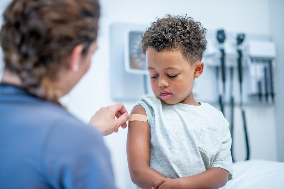 Doctor putting bandage on young boy's arm after vaccine